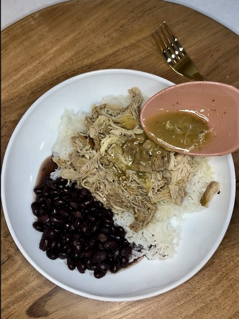 mojo juice being spooned over cooked chicken and rice on a plate next to black beans